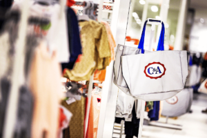 Foto de arara de roupas, com sacola com logo da C&A ao fundo