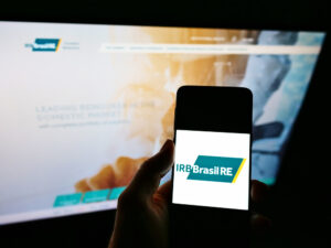 Foto de celular com logo do IRB e computador com site do IRB aberto ao fundo
