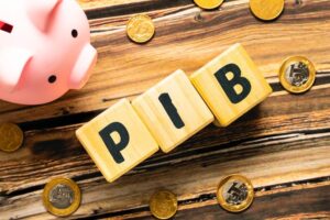 blocos com as letras PIB sobre mesa com moedas e cofre